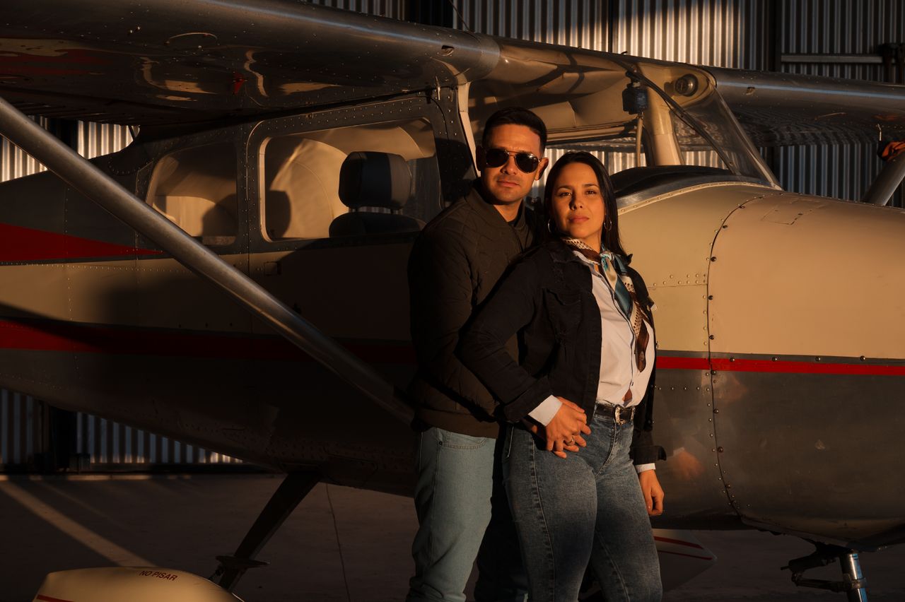 Couple posing in vintage aircraft hangar with small private plane and warm lighting.