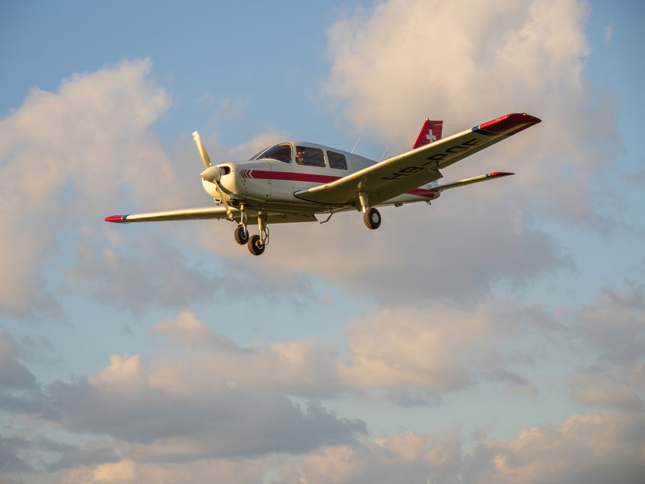 A light aircraft flying against a backdrop of clouds during the day, showcasing aviation in action.