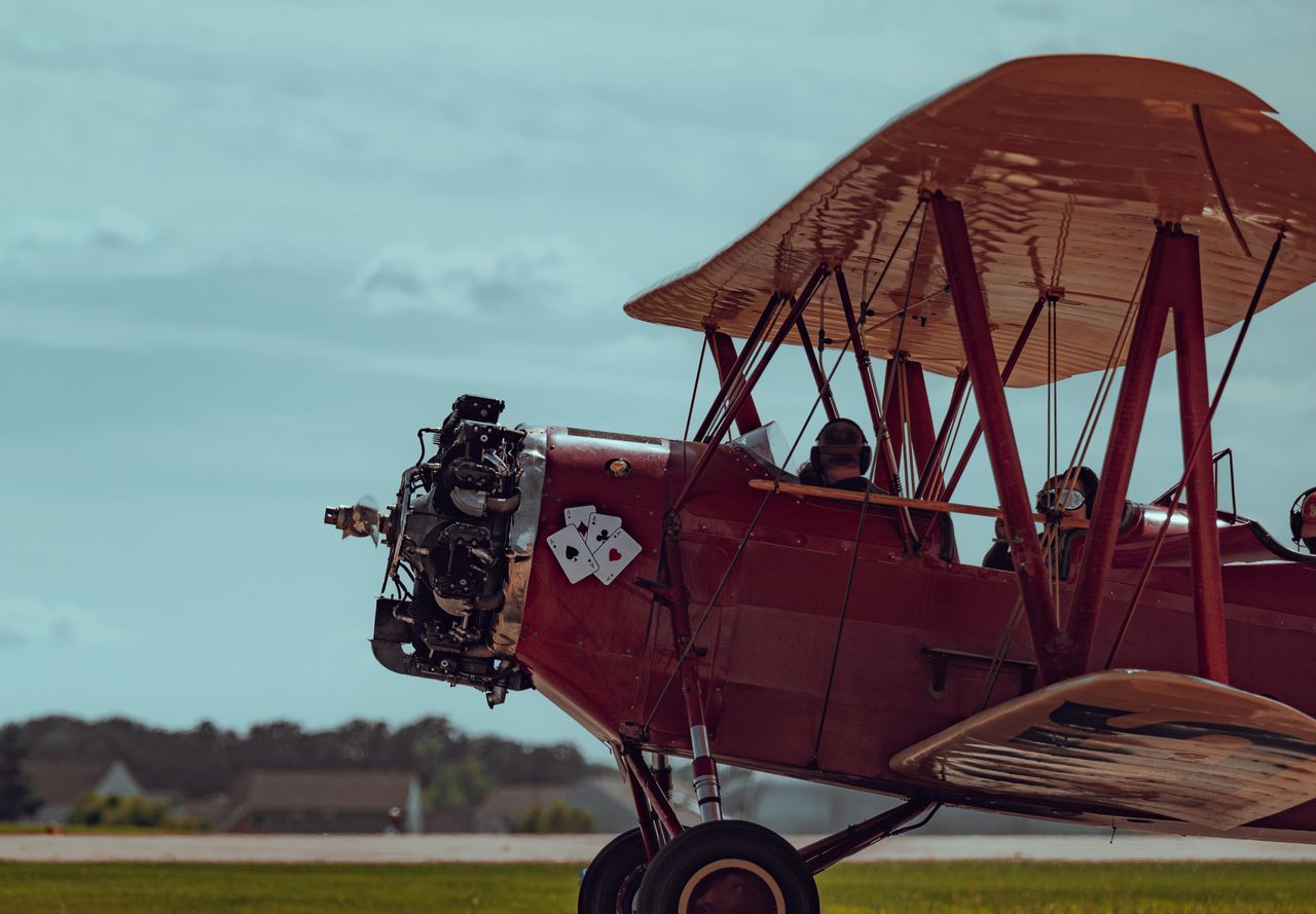 A classic red biplane soaring through the sky with pilots visible in the cockpit.